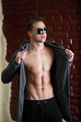 fashion boy with naked torso on the reed wall with sunglasses