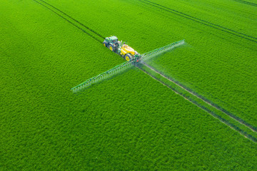 Green Fields. Aerial view of the tractor spraying the chemicals on the large green field....