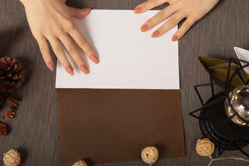Female hands with a white sheet of paper mock up on a cozy brown background with lights and a warm lamp