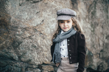 girl stands on the edge of a cliff near a large stone in a jacket