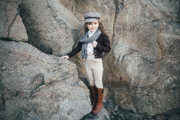 girl stands on the edge of a cliff near a large stone in a jacket