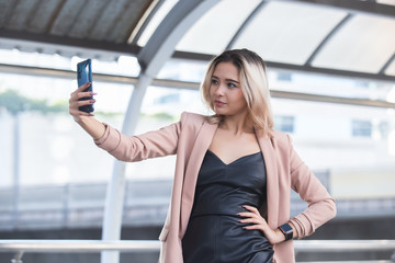 Young businesswoman using smartphone cheerful having video-call and photo selfie in city.