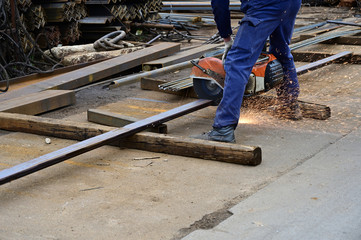Photo of a worker cutting metal reinforcement with a circular saw in the open air