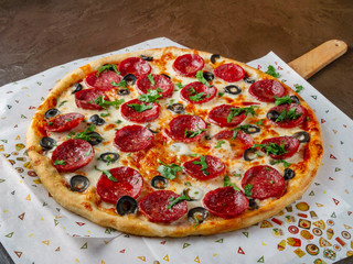Pizza with sausage lies on a serving paper sprinkled with chopped greens