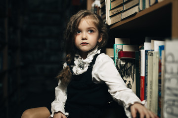 girl in a school uniform sits on a stool between shelves with books