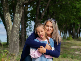 Fototapeta premium Happy young mother and daughter smile and kiss in nature on a warm Sunny day on Mother's Day.