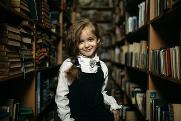girl in a school uniform stands between shelves with books