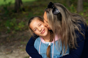 Naklejka premium Happy young mother and daughter smile and kiss in nature on a warm Sunny day on Mother's Day.