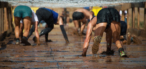 Runners crawling under a barbed wire in a test of the race, extreme obstacle race