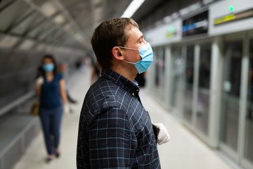 Male in protective medical mask is traveling and waiting train on platform in the metro.