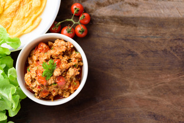 Northern Thai food (Nam Prik Ong), spicy chili minced pork with tomatoes in a bowl on wooden background, Thai chili paste, Top view