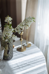 flowering branch with white flowers in a vase on a white table a glass and gold candlesticks