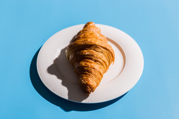 Bakery products baked croissant on white plate. Blue background, top view close-up. Pop art style. Summer shadows. Delicious and food concept.