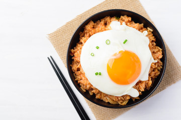 Kimchi fried rice with fried egg on top in a bowl and chopsticks on white table, Korean food, Top view