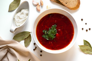 Beetroot soup in white bowl on a white table served with napkin, garlic, pepper, bread and saucy with sour cream. Traditional ukrainian, russian soup borscht with greens. Top view.