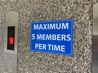 A sign warning message which has content is maximum five members per time is placed on a wall beside the elevator in an office during the pandemic of covid-19