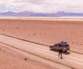 Obraz na płótnie Canvas Desert driving car. Mountain landscape. Driving down DRONE shot in Bolivia's Salt Flats. Couple in Salar de Uyuni salt flat. Dry landscape, empty. Holiday, vacation, driving, roadtrip, journey, road