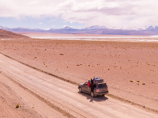 Desert driving car. Mountain landscape. Driving down DRONE shot in Bolivia's Salt Flats. Couple in Salar de Uyuni salt flat. Dry landscape, empty. Holiday, vacation, driving, roadtrip, journey, road