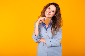 Joyful woman wears fashion pajama going to eat delicious cookie on yellow background with copy space. Morning, breakfast and home wear concept.