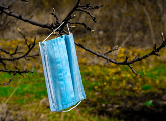 blue medical mask for individually protecting against the virus weighs on a tree branch....