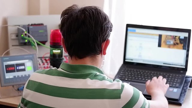 Back View of Young Man Who is Working Home Office and Making Online Education about PLC and Operator Panel Programming. Distance learning, also called distance education, e-learning or online learning
