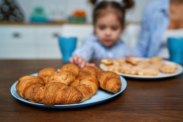 .Little girl wants to take croissant in the kitchen. Focus on sweet closeup.