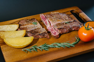 Succulent thick juicy portions of grilled fillet steak served with tomatoes and roast vegetables on an old wooden board