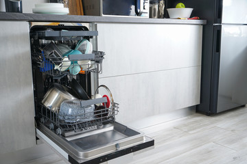 Dishwasher machine, open and loaded with dishes in the kitchen, after washing.