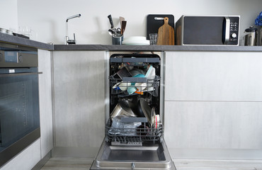 Dishwasher machine, open and loaded with dishes in the kitchen, after washing. Front view.