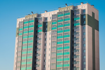 Fototapeta premium New multistorey panel home with balconies and windows, new building in sunlight on background blue sky.