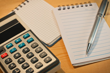 an old calculator black glasses a notepad a pencil on a yellow wooden board