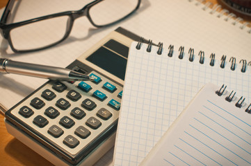 an old calculator black glasses a notepad a pencil on a yellow wooden board