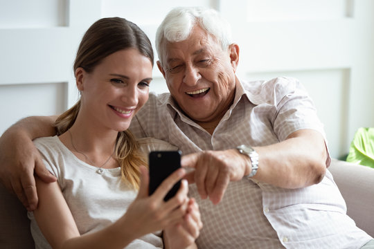 Happy mature 90s father and millennial girl child sit on couch smile making self-portrait picture on cell together, overjoyed senior dad and adult daughter have fun take selfie on smartphone at home