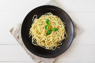 Pesto pasta on a black plate on a light background. Top view