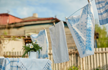 Wet white-blue laundry on clothesline to dry in the backyard. A wooden old house in the background.