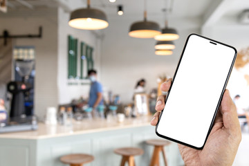Mockup image of hand holding smartphone with blank white screen in the coffee shop.