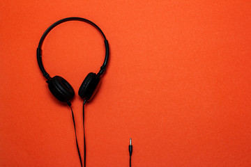 Black headphones in a minimalistic style on an orange paper background.