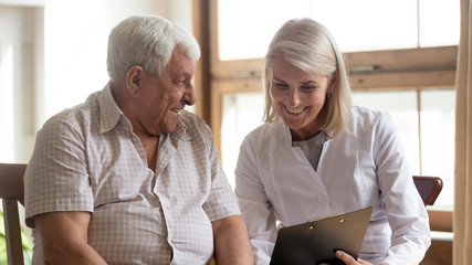 Smiling female nurse visit consult senior male patient in retirement house, positive woman doctor...