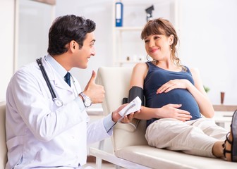 Young doctor checking pregnant woman's blood pressure
