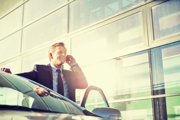 Portrait of Businessman standing outside his car while talking on smartphone