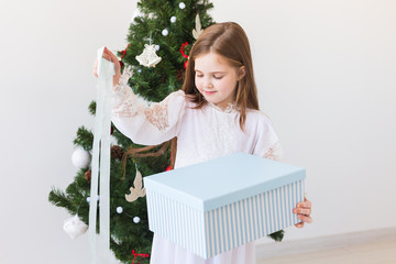 Child girl opens gift box near Christmas tree. Holidays, christmas time and presents concept.