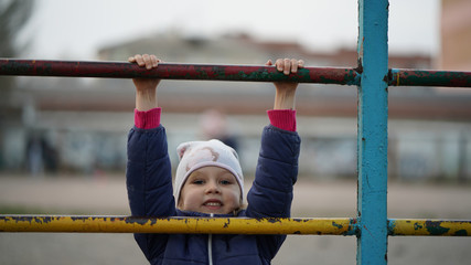 Obraz premium Portrait of cute little girl in white hat on playground do gymnastics exercises