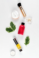 Cosmetics and self-care. A composition of green leaves, cream, brush, shower gel, perfume, oil in a tube and a candle are laid out on a white background. Flat lay. Vertical