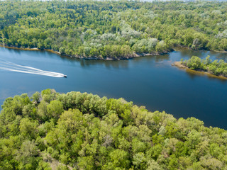 Obraz premium A motor boat floats on the Dnieper River in Kiev. Green trees on the banks of the river. Sunny spring day.