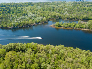 Obraz premium A motor boat floats on the Dnieper River in Kiev. Green trees on the banks of the river. Sunny spring day.