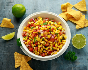 Mexican Corn Salsa in white bowl with lime and tortilla chips. Healthy food