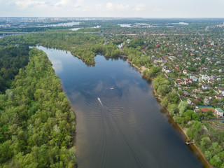 A motor boat floats on the Dnieper River in Kiev. Green trees on the banks of the river. Sunny spring day.