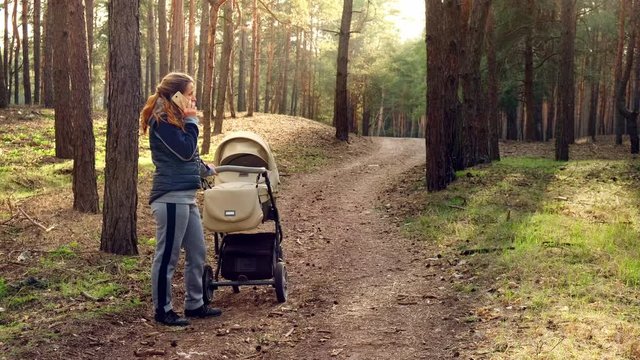 A woman with a stroller walks in the spring forest in the fresh air and is not afraid of viruses. Mom walks in the woods with a small child and talks on the phone. 4K UHD video camera, 2x slow motion.