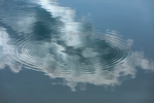 Reflection of cloud and blue sky on mirror smooth water. Concentric circles define the surface of the water