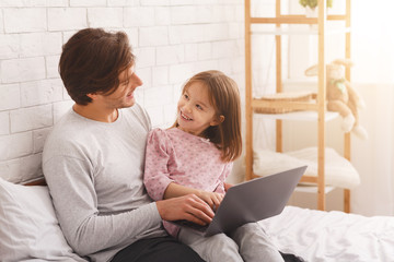 Father and daughter using laptop in bedroom